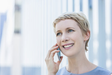 Porträt einer lächelnden blonden Frau, die mit einem Smartphone telefoniert - TCF004316