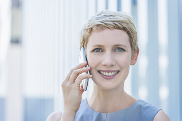 Porträt einer lächelnden blonden Frau, die mit einem Smartphone telefoniert - TCF004317