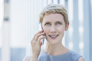 Porträt einer lächelnden blonden Frau, die mit einem Smartphone telefoniert und nach oben schaut - TCF004318