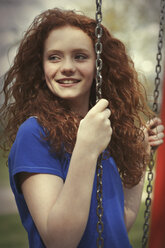 Porträt eines lächelnden Mädchens mit lockigem rotem Haar, das auf einer Schaukel sitzt - GDF000409
