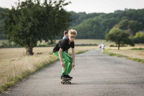 Junge fährt Skateboard auf einer Landstraße - PAF000859