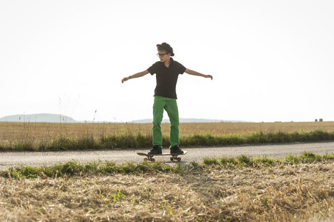 Junge steht auf seinem Skateboard vor einem Stoppelfeld, lizenzfreies Stockfoto