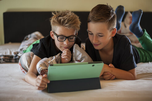 Zwei Jungen liegen auf dem Bett und benutzen ein digitales Tablet - PAF000861