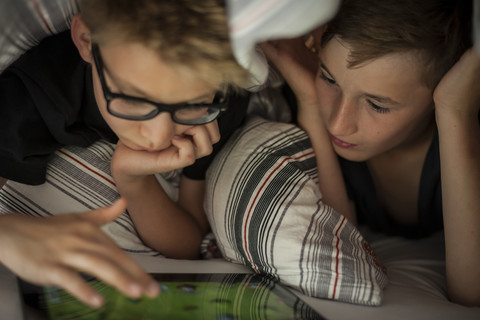 Two boys lying on bed using digital tablet stock photo