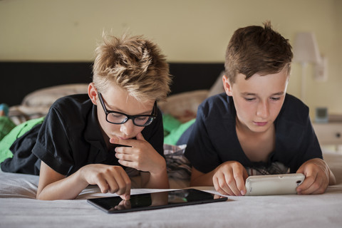 Zwei Jungen liegen auf dem Bett und benutzen ein digitales Tablet, lizenzfreies Stockfoto