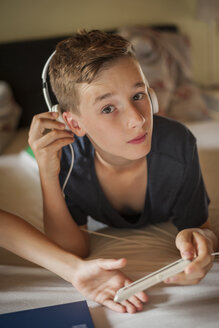Porträt eines auf dem Bett liegenden Jungen, der mit Kopfhörern Musik hört - PAF000866