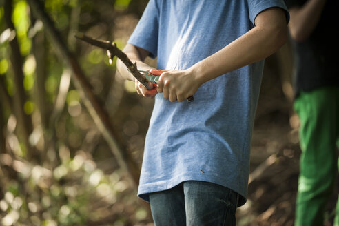 Junge schnitzt Zweige mit seinem Taschenmesser in einem Wald, Teilansicht - PAF000878
