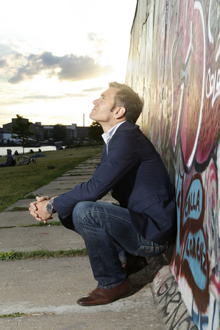 Deutschland, Berlin, Geschäftsmann hockt an der Berliner Mauer, nachdenklich, lizenzfreies Stockfoto