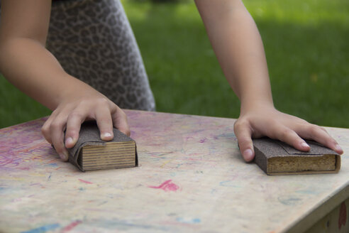 Mädchenhände arbeiten auf einem Holztisch mit Sandpapierblöcken - YFF000227