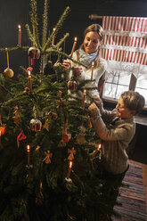 Mother and her little son lightning candles of a Christmas tree in a farmhouse - HHF004857