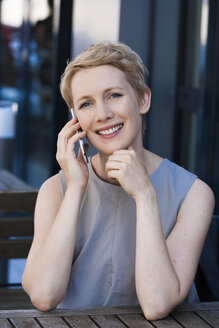 Porträt einer lächelnden blonden Frau, die mit einem Smartphone telefoniert - TCF004441