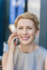 Porträt einer lächelnden blonden Frau, die mit einem Smartphone telefoniert - TCF004442