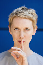 Portrait of blond woman with finger on her mouth in front of blue background - TCF004450