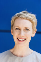 Porträt einer lächelnden blonden Frau vor einem blauen Hintergrund - TCF004452