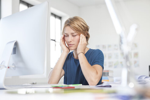 Portrait of young woman with headache at her desk in a creative office - RBF001808