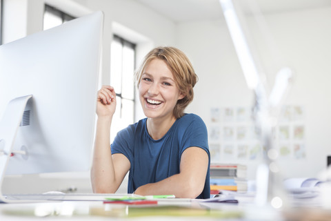 Porträt einer glücklichen jungen Frau an ihrem Schreibtisch in einem kreativen Büro, lizenzfreies Stockfoto