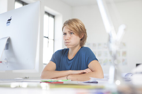 Porträt einer jungen Frau, die an ihrem Schreibtisch in einem kreativen Büro einen Schmollmund zieht - RBF001811