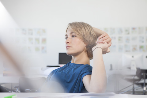 Porträt einer nachdenklichen jungen Frau an ihrem Schreibtisch in einem kreativen Büro, lizenzfreies Stockfoto