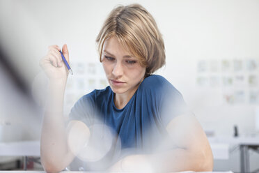 Portrait of pensive young woman at her desk in a creative office - RBF001838