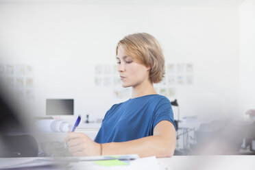 Portrait of pensive young woman at her desk in a creative office - RBF001844