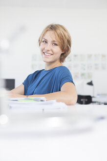 Porträt einer lächelnden jungen Frau an ihrem Schreibtisch in einem kreativen Büro - RBF001845