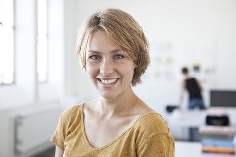 Porträt einer lächelnden jungen Frau in einem kreativen Büro, lizenzfreies Stockfoto