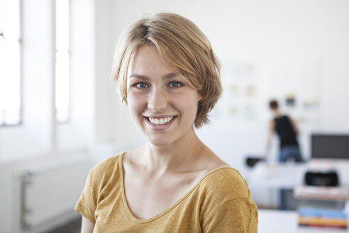 Porträt einer lächelnden jungen Frau in einem kreativen Büro - RBF001813