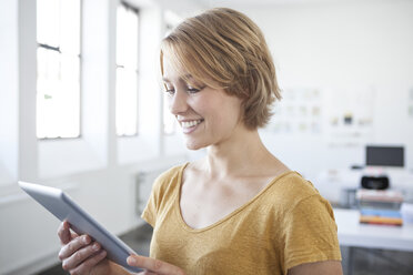 Porträt einer lächelnden jungen Frau mit digitalem Tablet in einem kreativen Büro - RBF001814