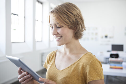 Porträt einer lächelnden jungen Frau mit digitalem Tablet in einem kreativen Büro - RBF001814