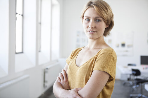 Porträt einer jungen Frau mit verschränkten Armen in einem kreativen Büro - RBF001815