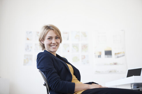 Porträt einer lächelnden jungen Frau an ihrem Schreibtisch in einem kreativen Büro - RBF001847