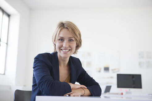 Porträt einer lächelnden jungen Frau an ihrem Schreibtisch in einem kreativen Büro - RBF001848