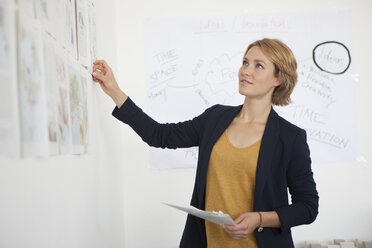 Porträt einer jungen Frau, die eine Wand mit Konzepten in einem Büro betrachtet - RBF001849