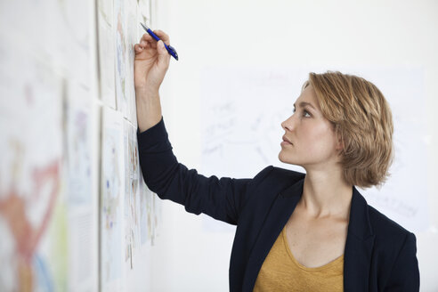 Porträt einer jungen Frau mit Blick auf eine Wand mit Konzepten in einem Büro - RBF001852