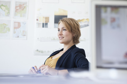 Porträt einer lächelnden jungen Frau an ihrem Schreibtisch in einem kreativen Büro, lizenzfreies Stockfoto