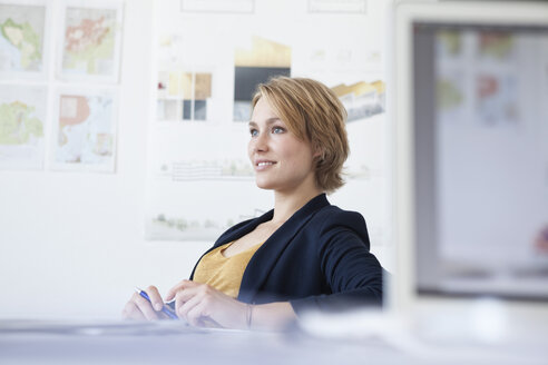 Porträt einer lächelnden jungen Frau an ihrem Schreibtisch in einem kreativen Büro - RBF001854