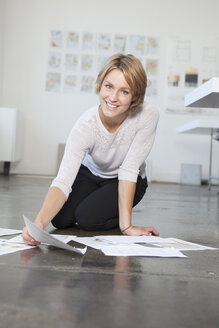 Porträt einer jungen Frau, die mit ihren Konzepten auf dem Boden eines Büros sitzt - RBF001858