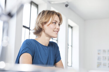 Smiling young woman at her desk in a creative office - RBF001818