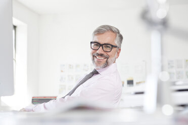 Porträt eines lächelnden Mannes an seinem Schreibtisch in einem Büro - RBF001827