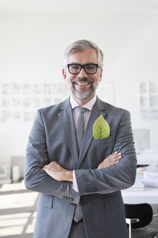 Porträt eines lächelnden Geschäftsmannes mit grünem Blatt in seiner Jackentasche, lizenzfreies Stockfoto