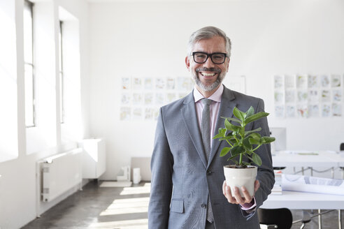 Porträt eines lächelnden Geschäftsmannes mit Blumentopf in einem Büro - RBF001882