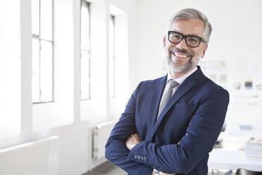 Portrait of smiling businessman with crossed arms in an office - RBF001884