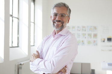 Portrait of smiling businessman with crossed arms in an office - RBF001896