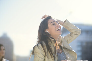 Portrait of laughing woman with earphones listening music - ZEF000774