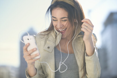 Porträt einer lachenden Frau mit Smartphone und Kopfhörern beim Musikhören - ZEF000777