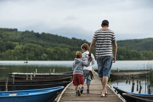 Germany, Rhineland-Palatinate, Laacher See, father walking with two sons on jetty - PAF000920