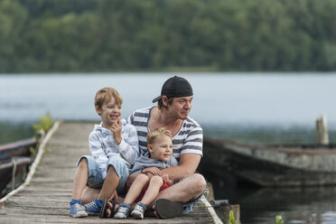 Germany, Rhineland-Palatinate, Laacher See, father sitting with two sons on jetty - PAF000921