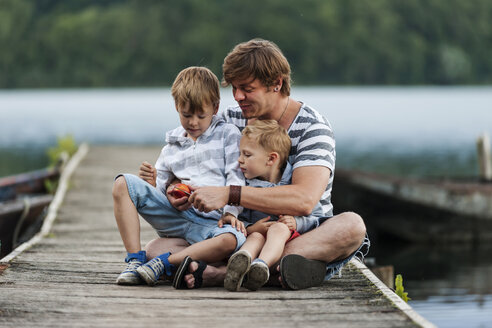 Deutschland, Rheinland-Pfalz, Laacher See, Vater sitzt mit zwei Söhnen am Steg - PAF000923