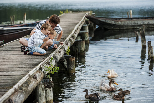 Deutschland, Rheinland-Pfalz, Laacher See, Vater mit zwei Söhnen am Steg beim Füttern von Enten - PAF000924