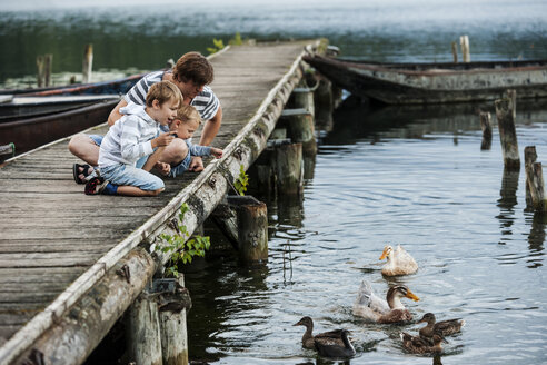 Germany, Rhineland-Palatinate, Laacher See, father with two sons on jetty feeding ducks - PAF000924